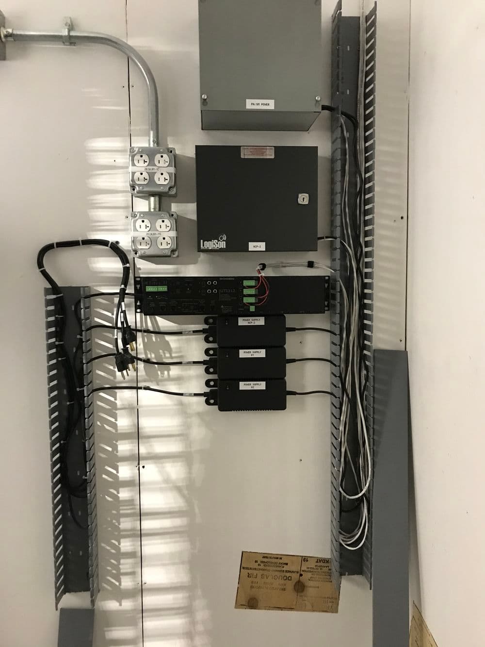 Network equipment mounted on wall, featuring routers, cables, and power connections.
