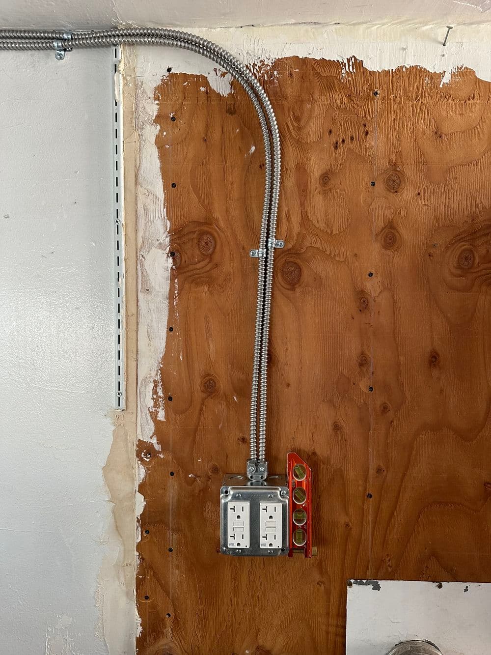 Electrical outlet installation on wooden wall with conduit and level tool visible.