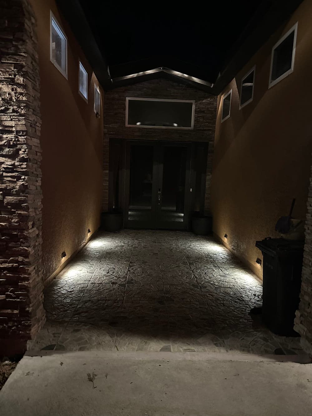Modern home entrance with stone walls, nighttime lighting, and a trash bin.