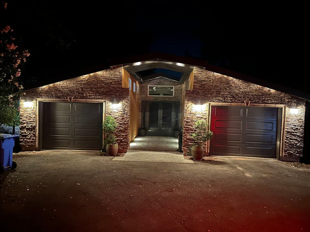 Modern house exterior at night with stone facade and illuminated entrance.