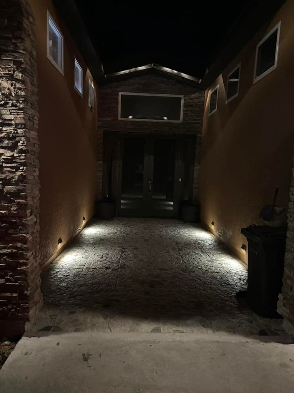 Illuminated entryway with stone walls leading to a modern front door at night.