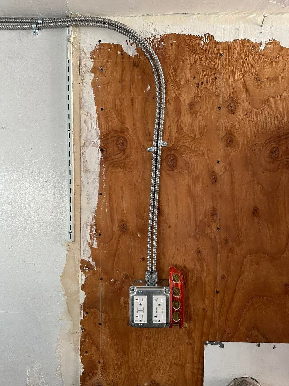 Electrical wall outlet installation with conduit and level, against a wooden surface.